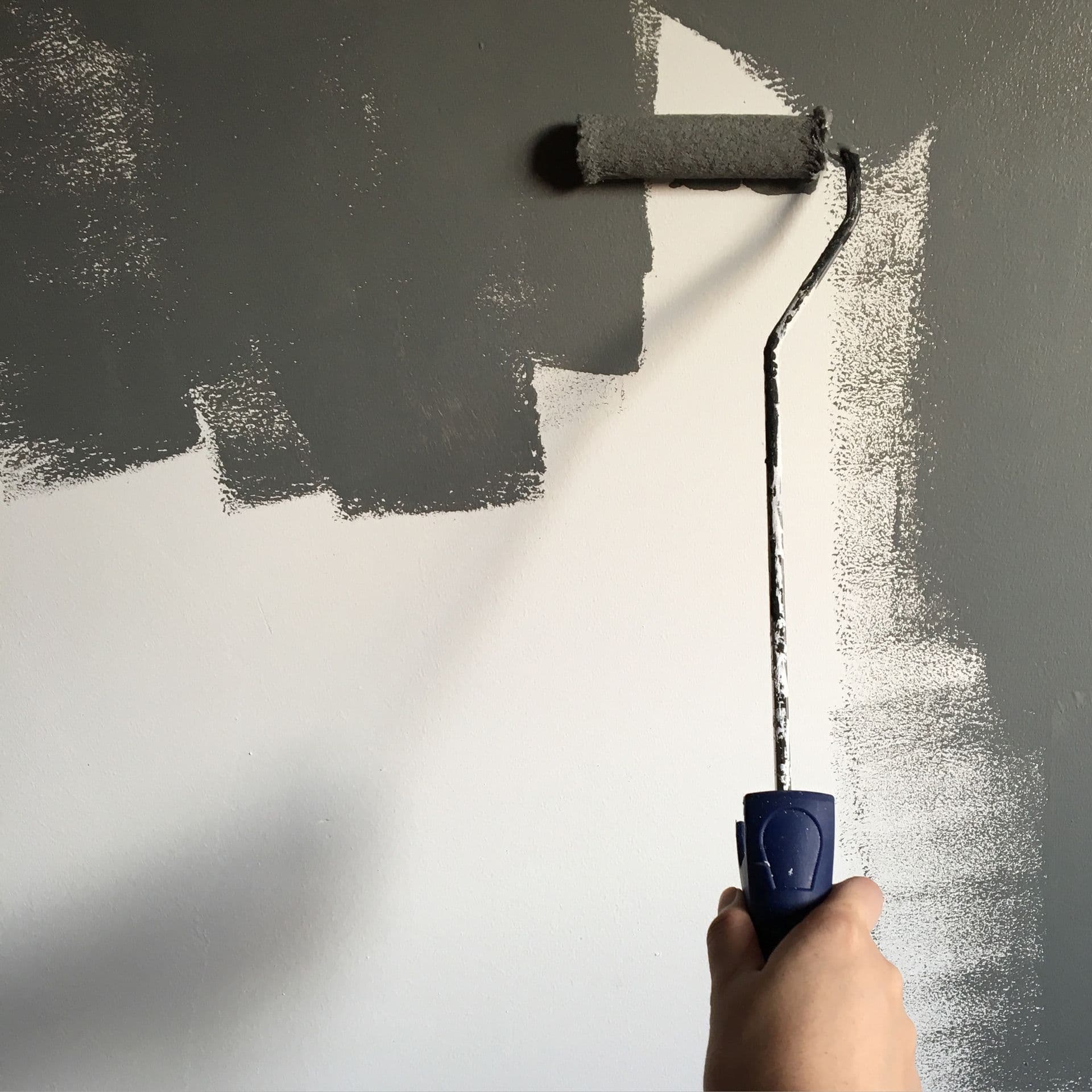 A hand rolling warm gray paint onto an interior wall